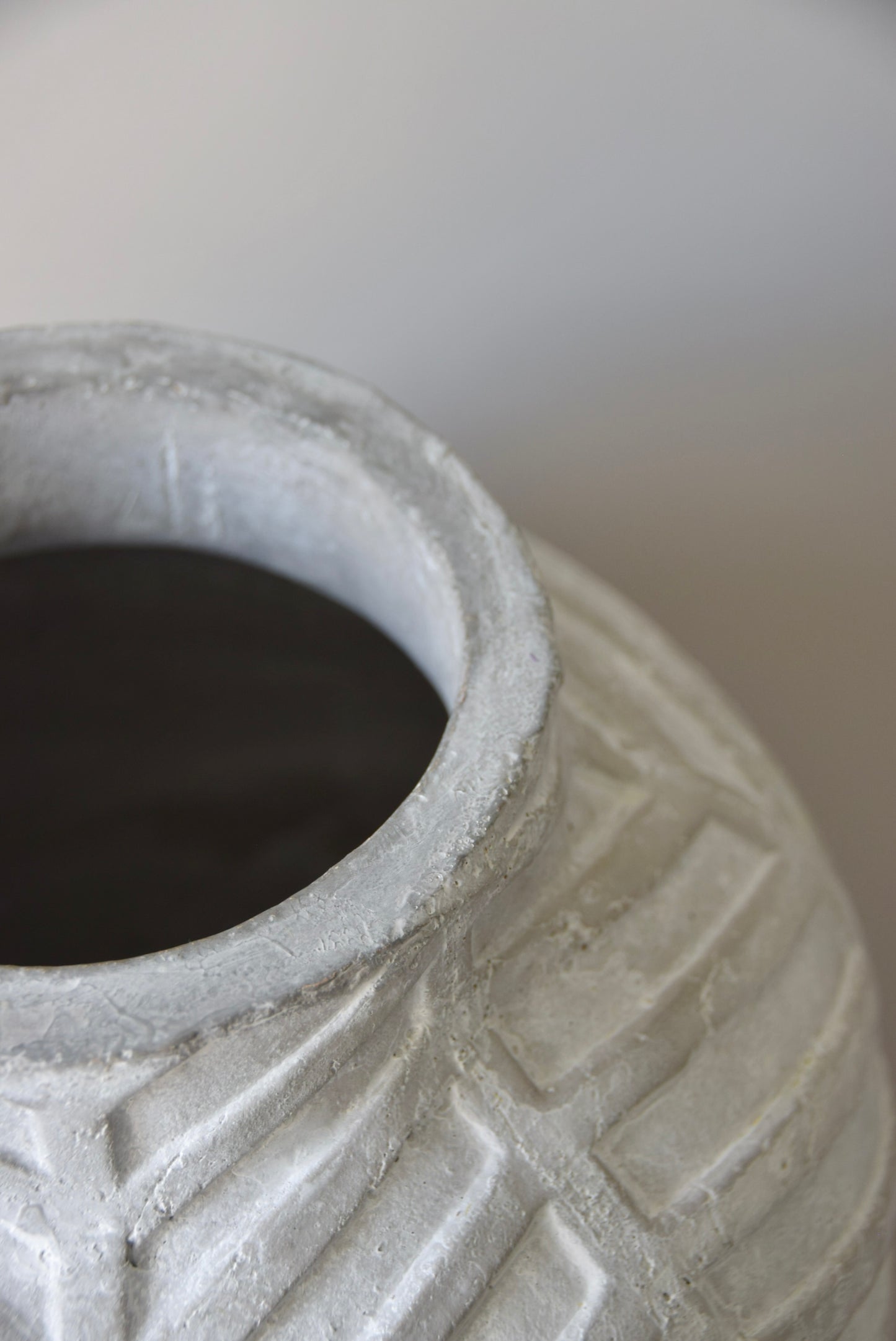 Grey chevron stone ceramic vase displayed on a black pedestal against a beige wall.