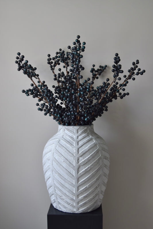Stone chevron style vase placed on a black pedestal displaying some blueberry stems.
