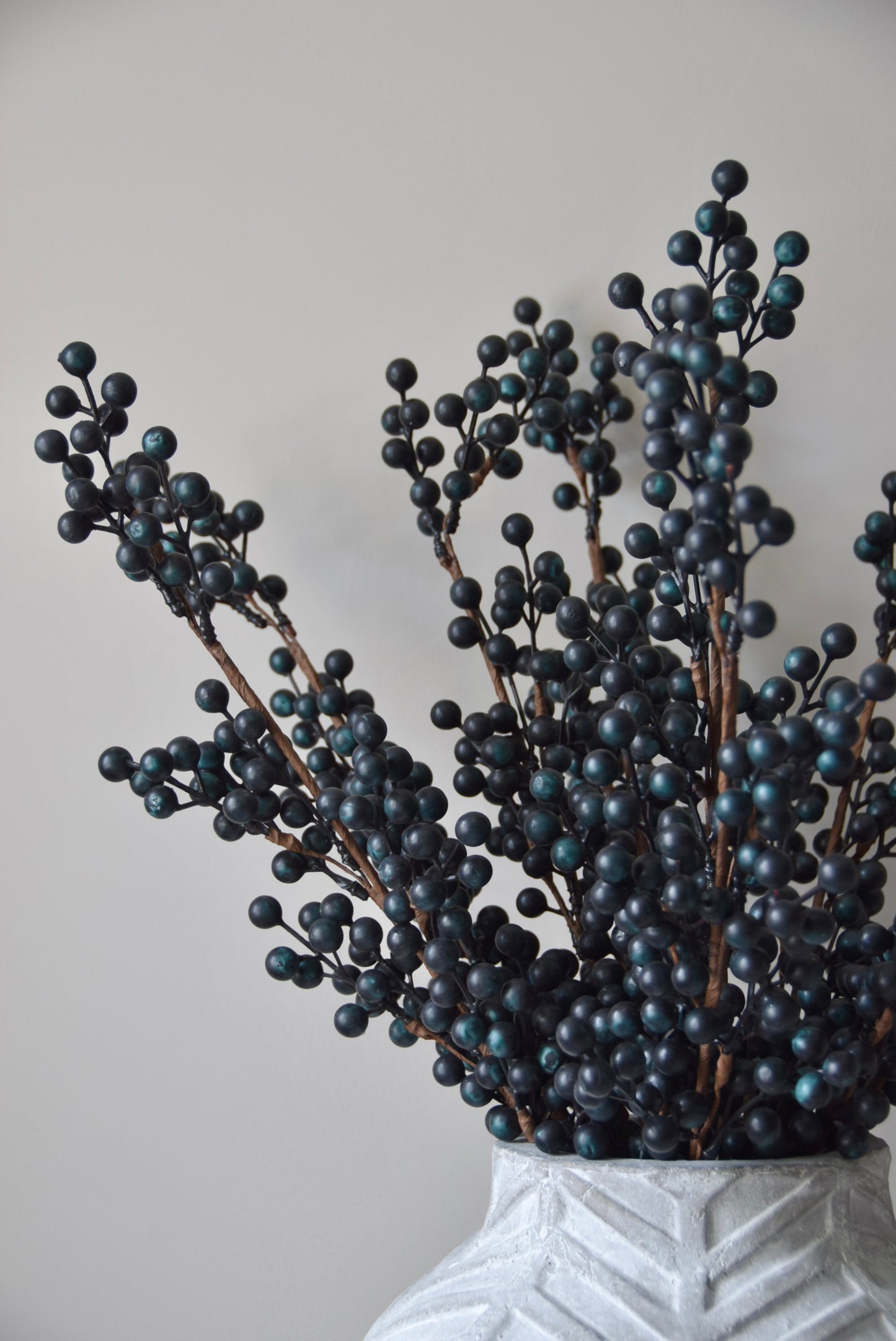Stone chevron style vase placed on a black pedestal displaying some blueberry stems.