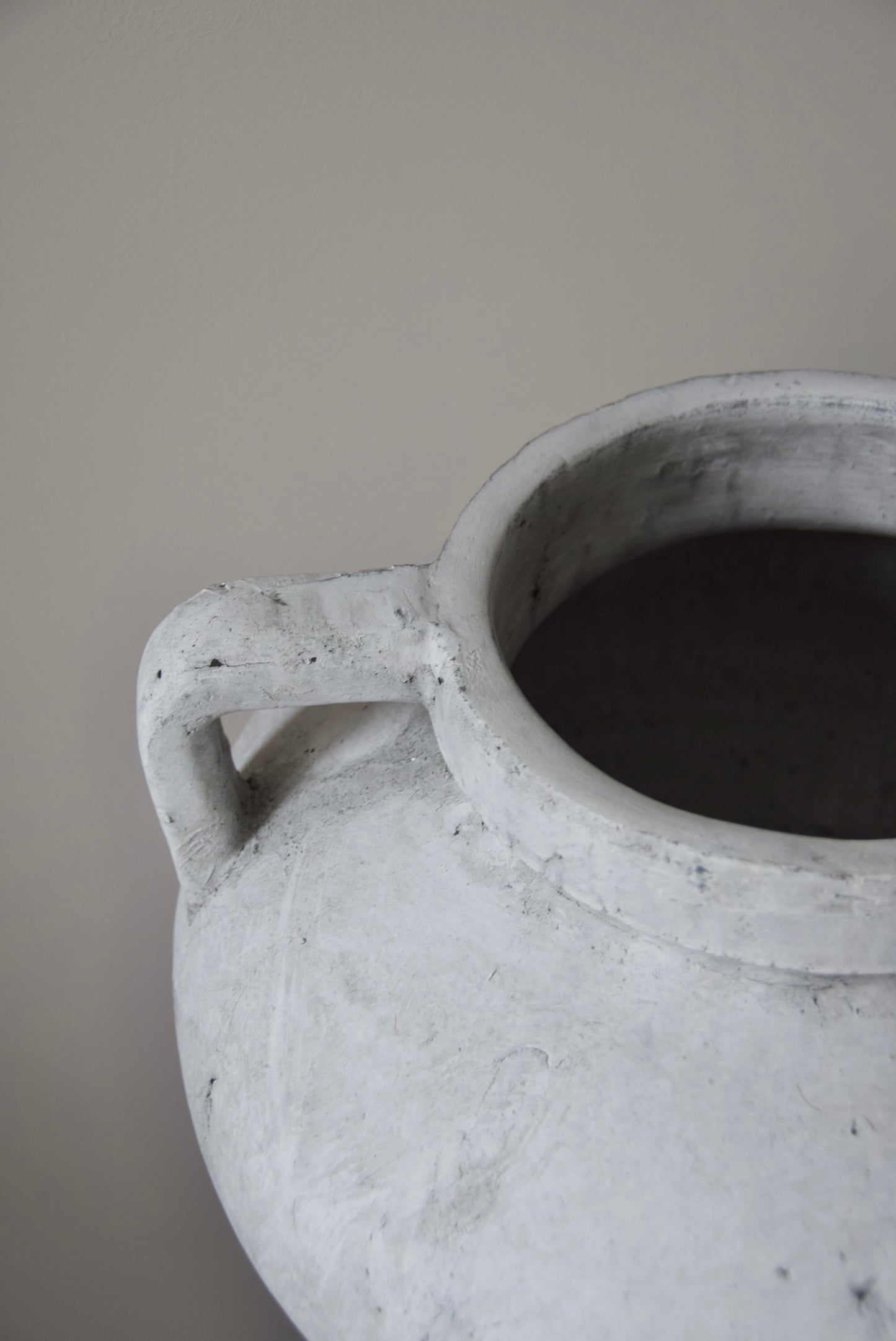 Grey stone Greek pelike vase with two handles displayed on a black pedestal.