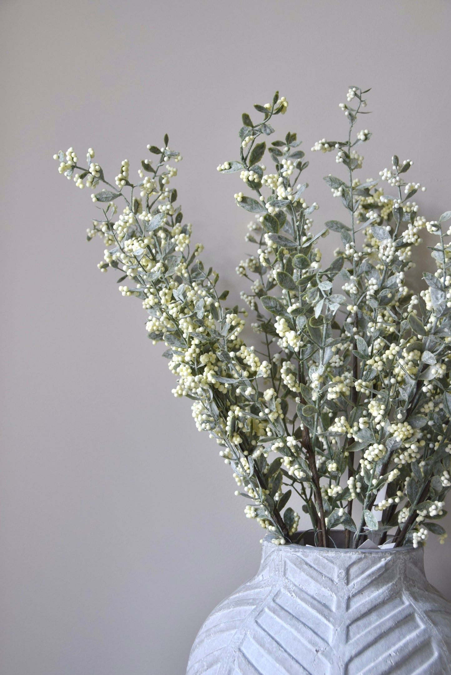 Stone chevron style vase placed on a black pedestal displaying a bunch of artificial berry leaf stems.