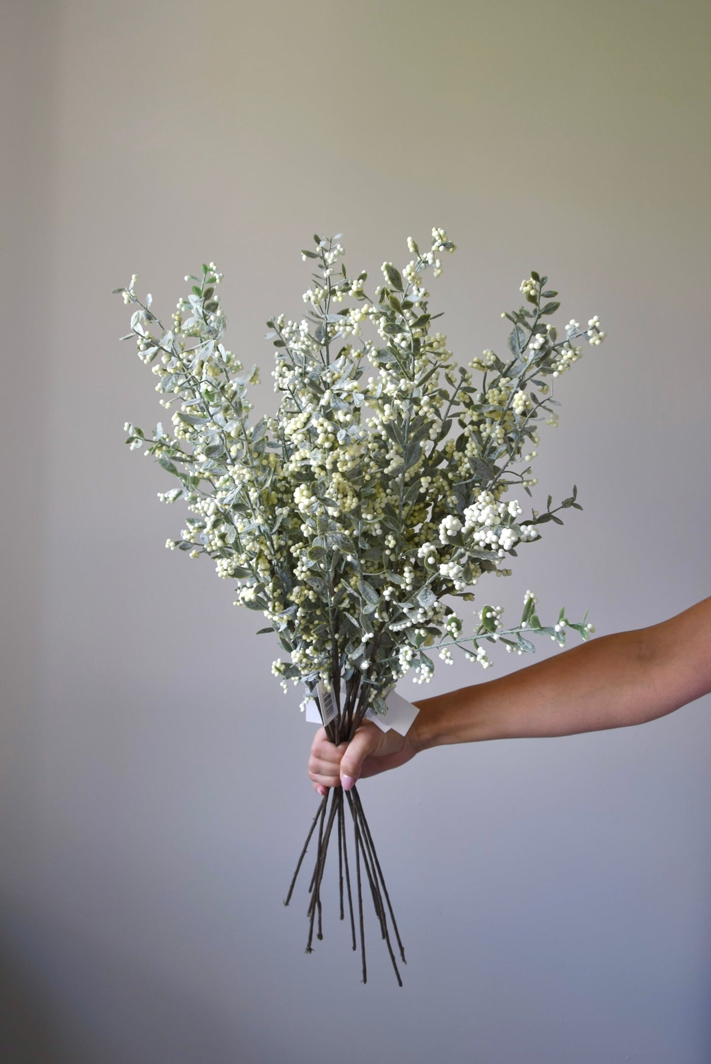 A bunch of artificial berry leaf stems being held against a neutral coloured wall.