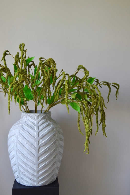 Stone chevron vase placed on a black pedestal displaying a bunch of artificial green catkin stems.