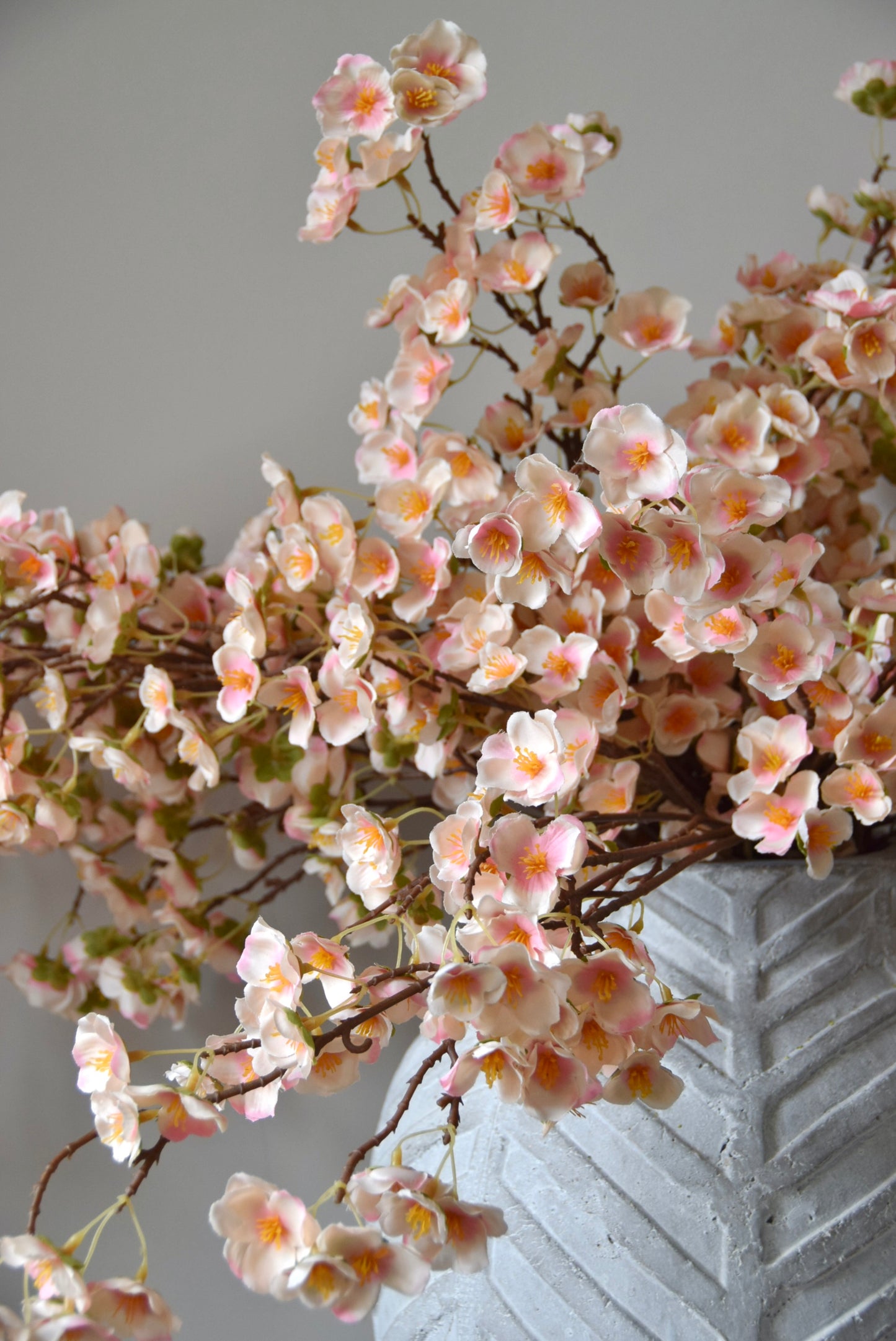 Stone chevron style vase placed on a black pedestal with a bunch of drooping pink plum blossom stems.