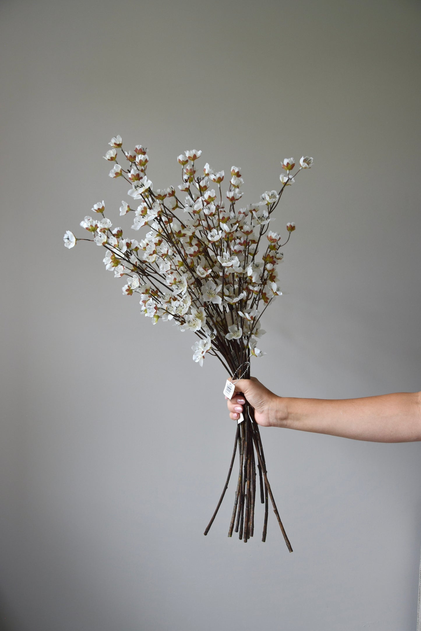 A bunch of artificial cherry blossom branches displayed against a neutral coloured wall.