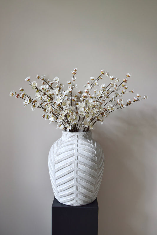 Stone chevron style vase placed on a black pedestal displaying a bunch of artificial cherry blossom branches.