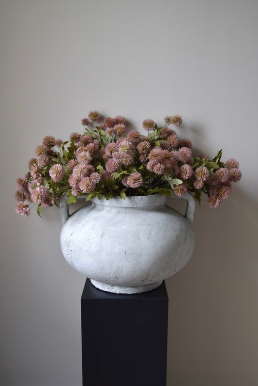 White vase with pink flowers on a black pedestal against a plain background