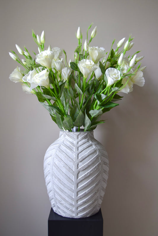 White vase with a textured pattern containing a bouquet of white flowers on a plain background