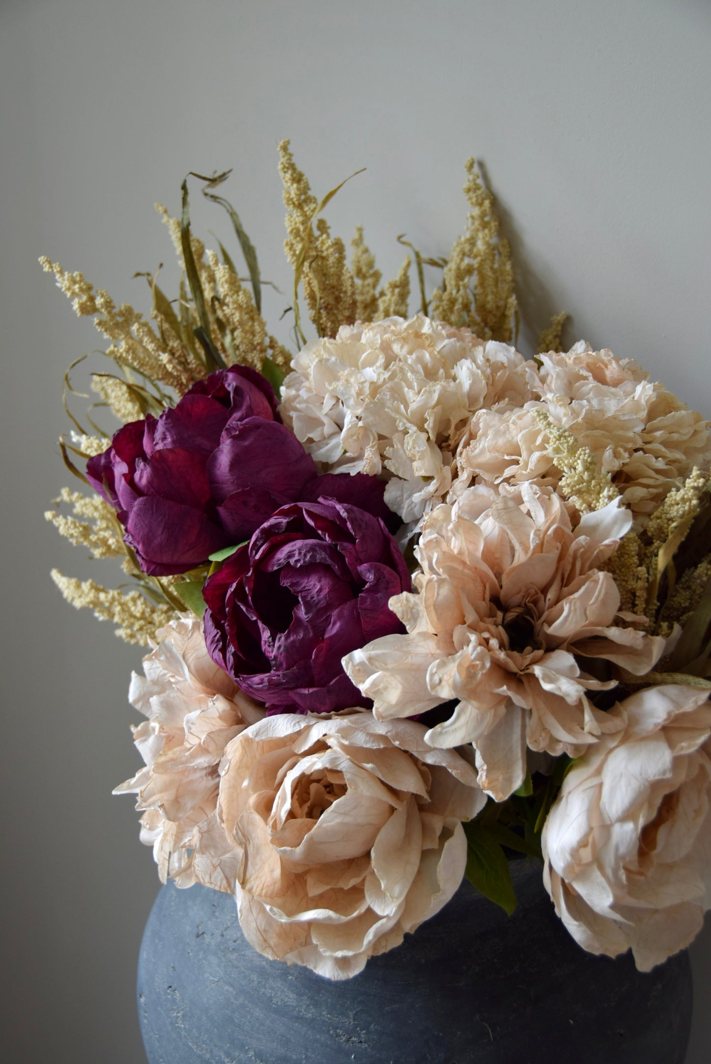 Bouquet of flowers with purple and beige roses in a grey vase against a neutral background