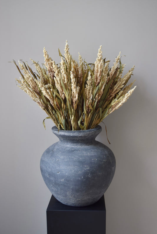 Grey vase with dried plants on a black stand against a neutral background