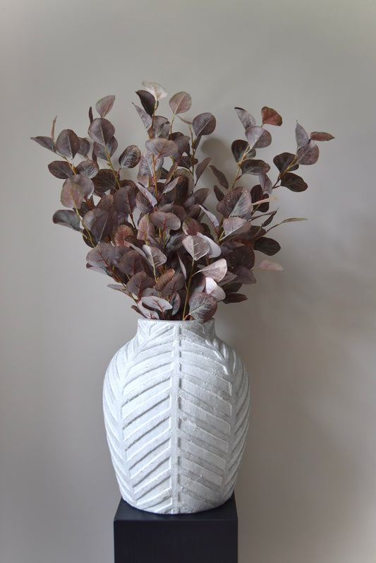 White textured vase with dried eucalyptus against a plain background