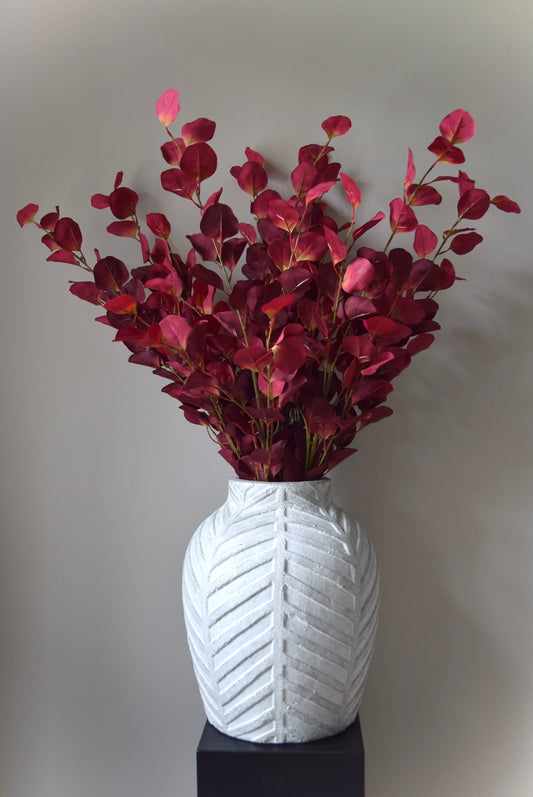 White textured vase with red leaves on a plain background