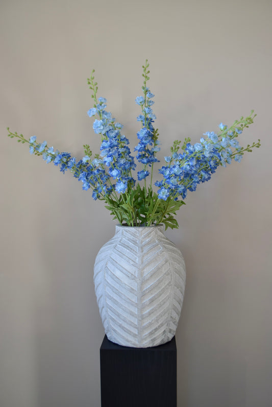 A bunch of artificial blue delphinium stems displayed in a stone chevron style vase.