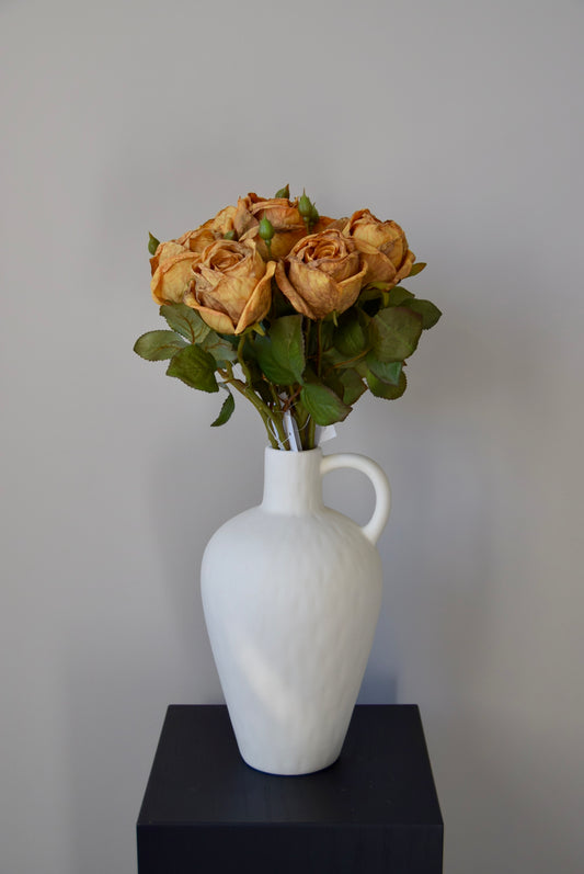 White vase with dried roses on a black surface against a grey background
