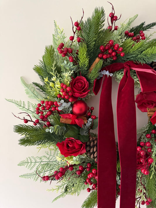 Decorative wreath with red ribbons, roses, and berries on a light background