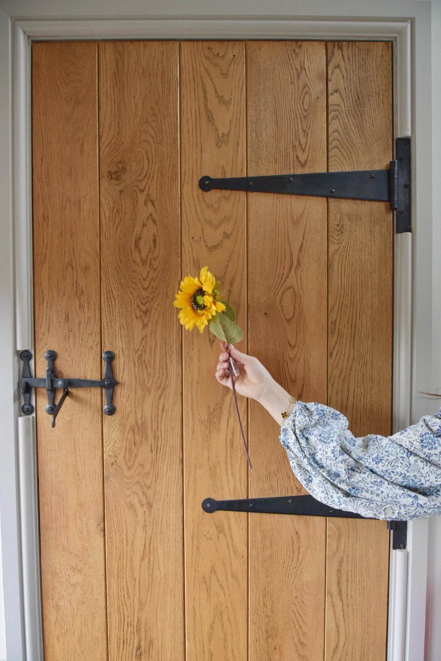 Artificial yellow sunflower stem displayed against a country style wooden door.