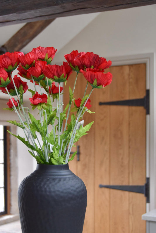 Tall black vase placed on a kitchen countertop with a bunch of tall red country poppies. Displayed in a country style kitchen for home decor.