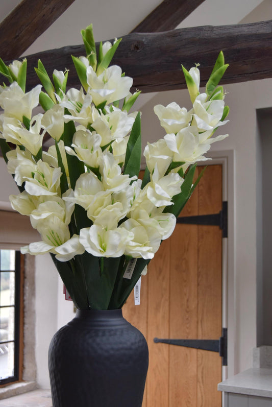 Tall black vase placed on a kitchen countertop with a bunch of gladioli stems. Displayed in a country style kitchen for home decor.