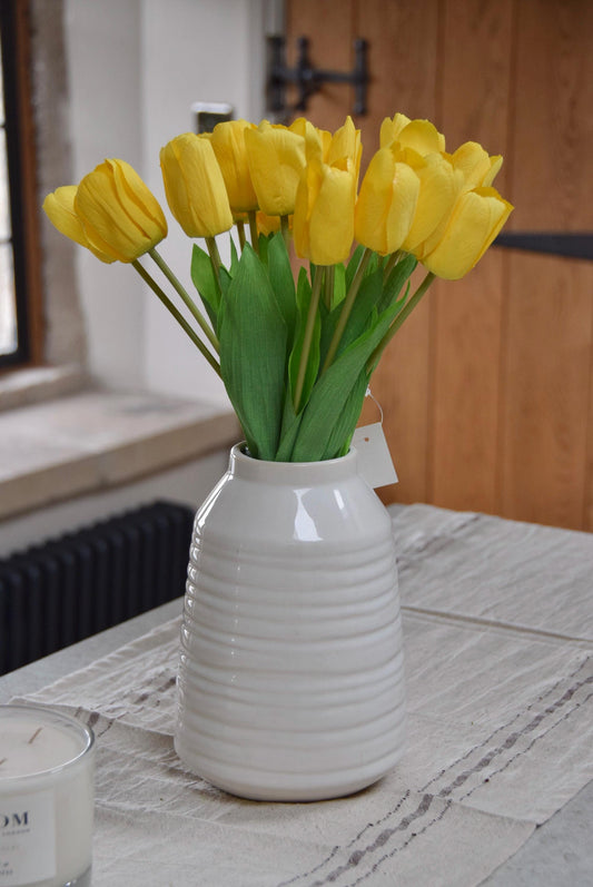 Yellow tulips set in a cream vase on a kitchen counter top in a country style kitchen for home decor