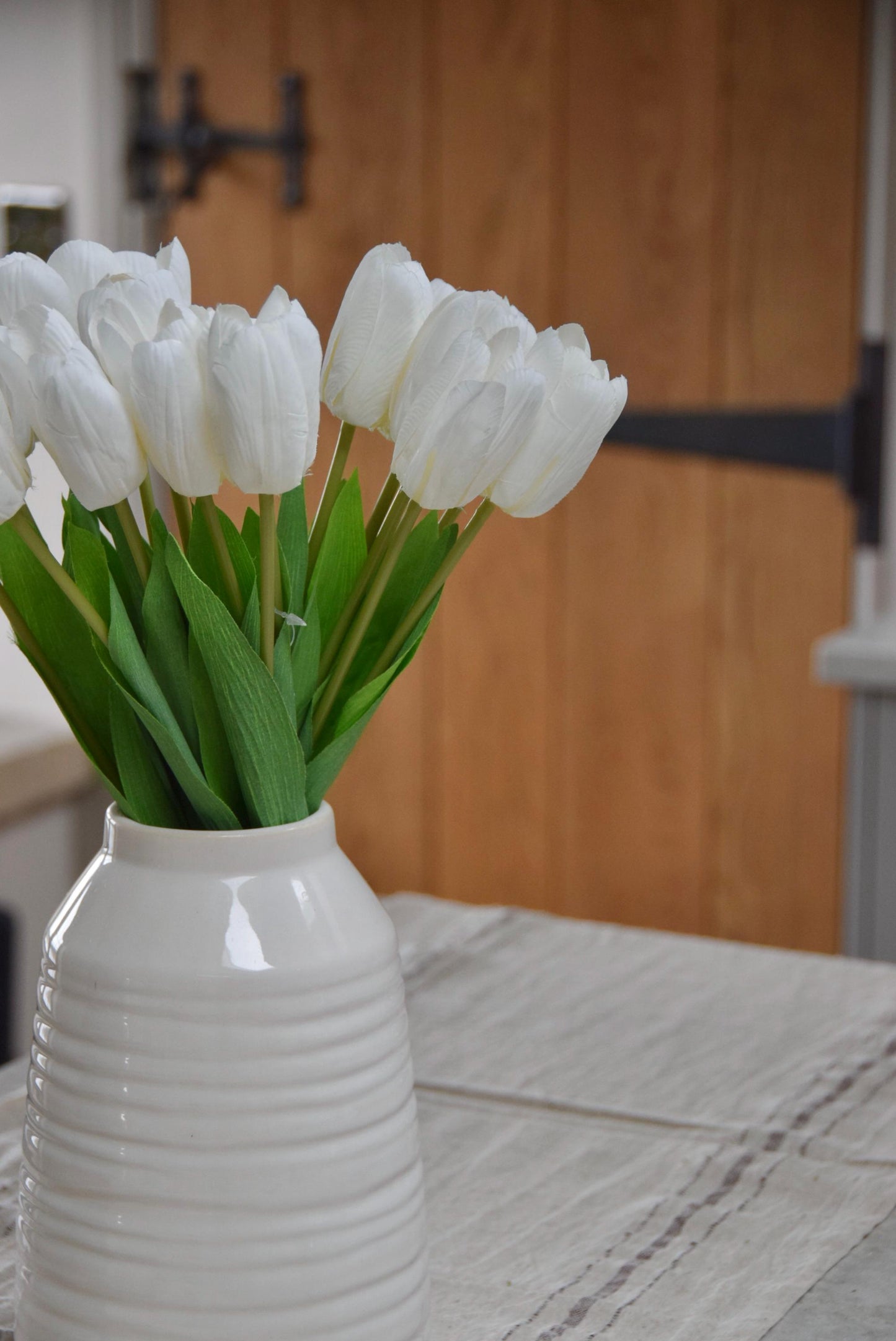 White tulips set in a cream vase on a kitchen counter top in a country style kitchen for home decor