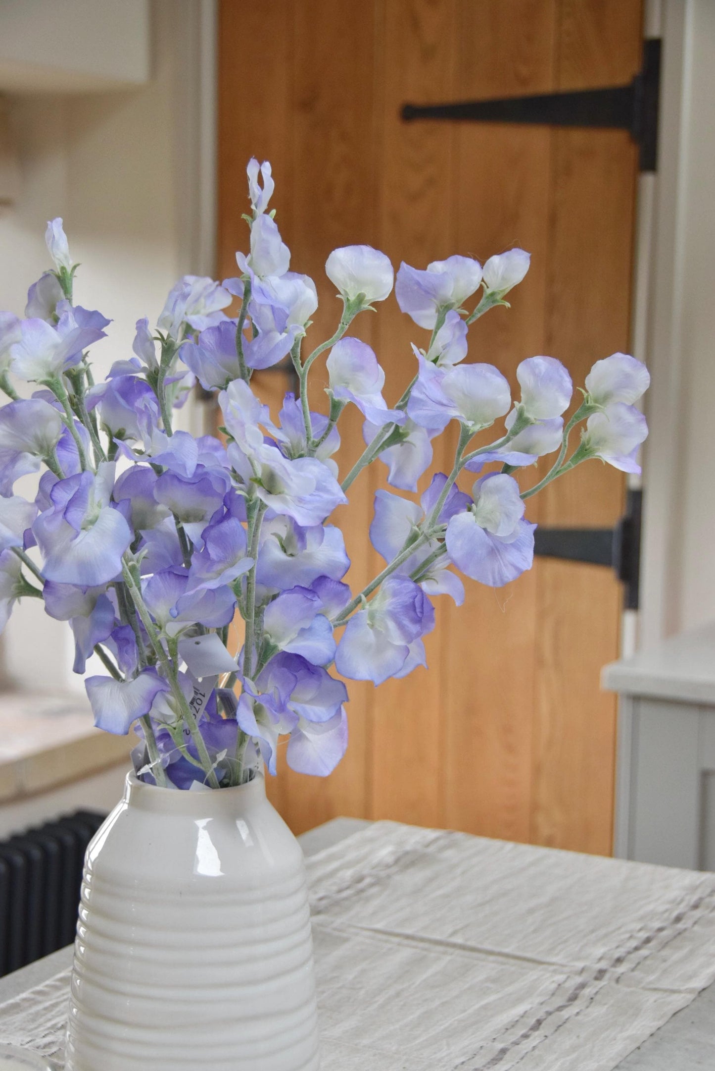 Lilac sweet peas set in a cream vase on a kitchen countertop in a country style house for home decor.