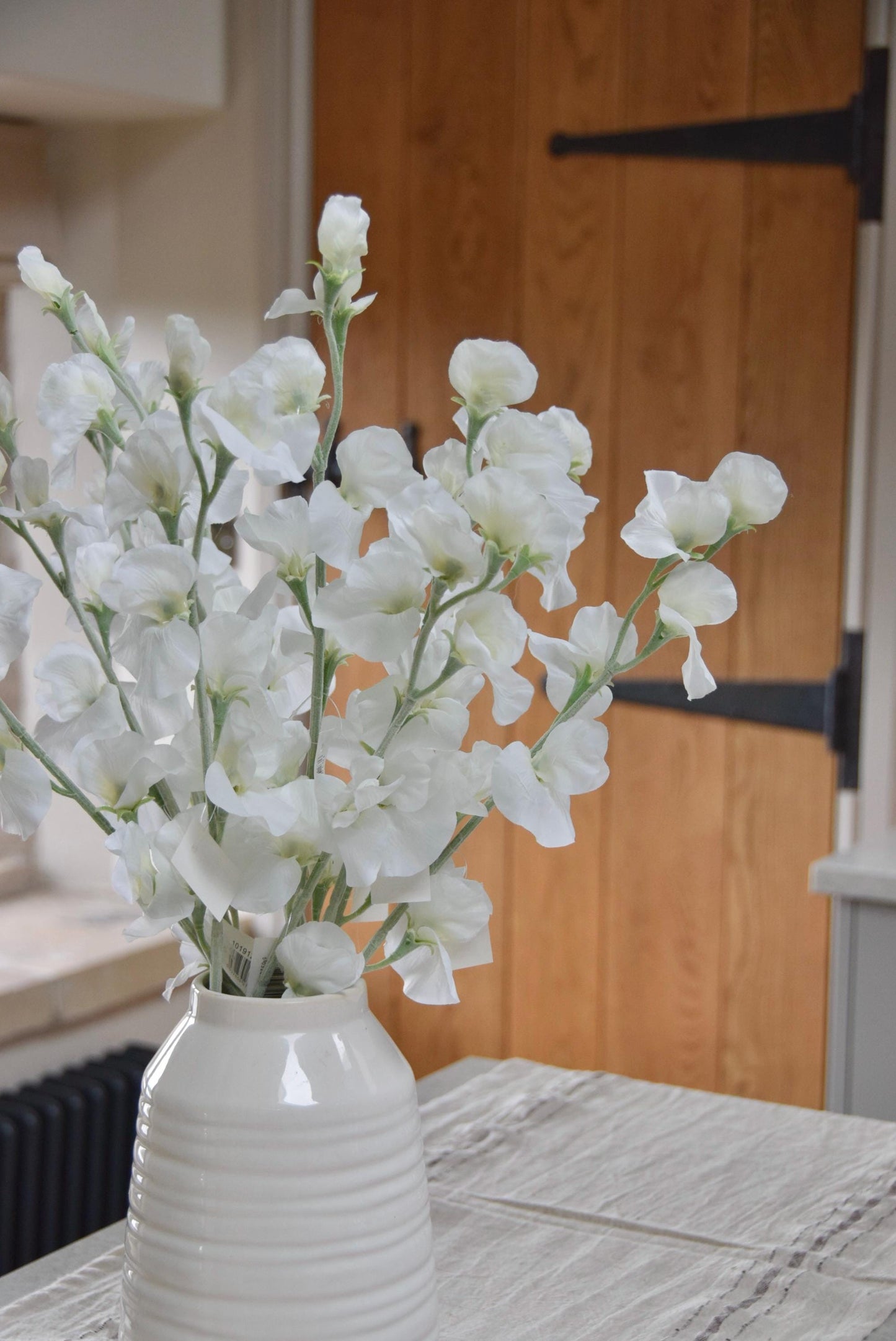 White sweet peas set in a cream vase on a kitchen countertop in a country style house for home decor.