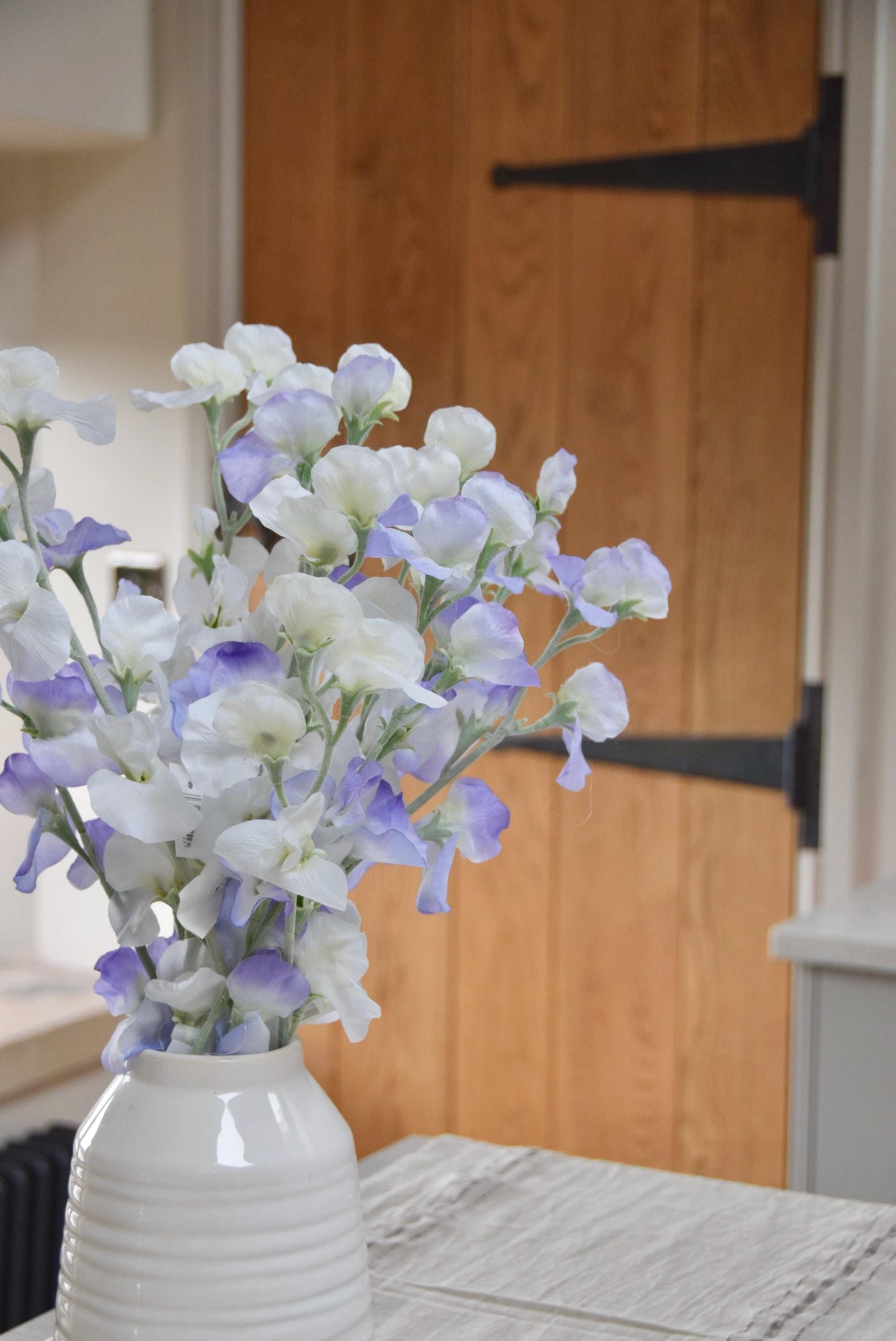 Lilac and white sweet peas set in a cream vase on a kitchen countertop in a country style kitchen for home decor.