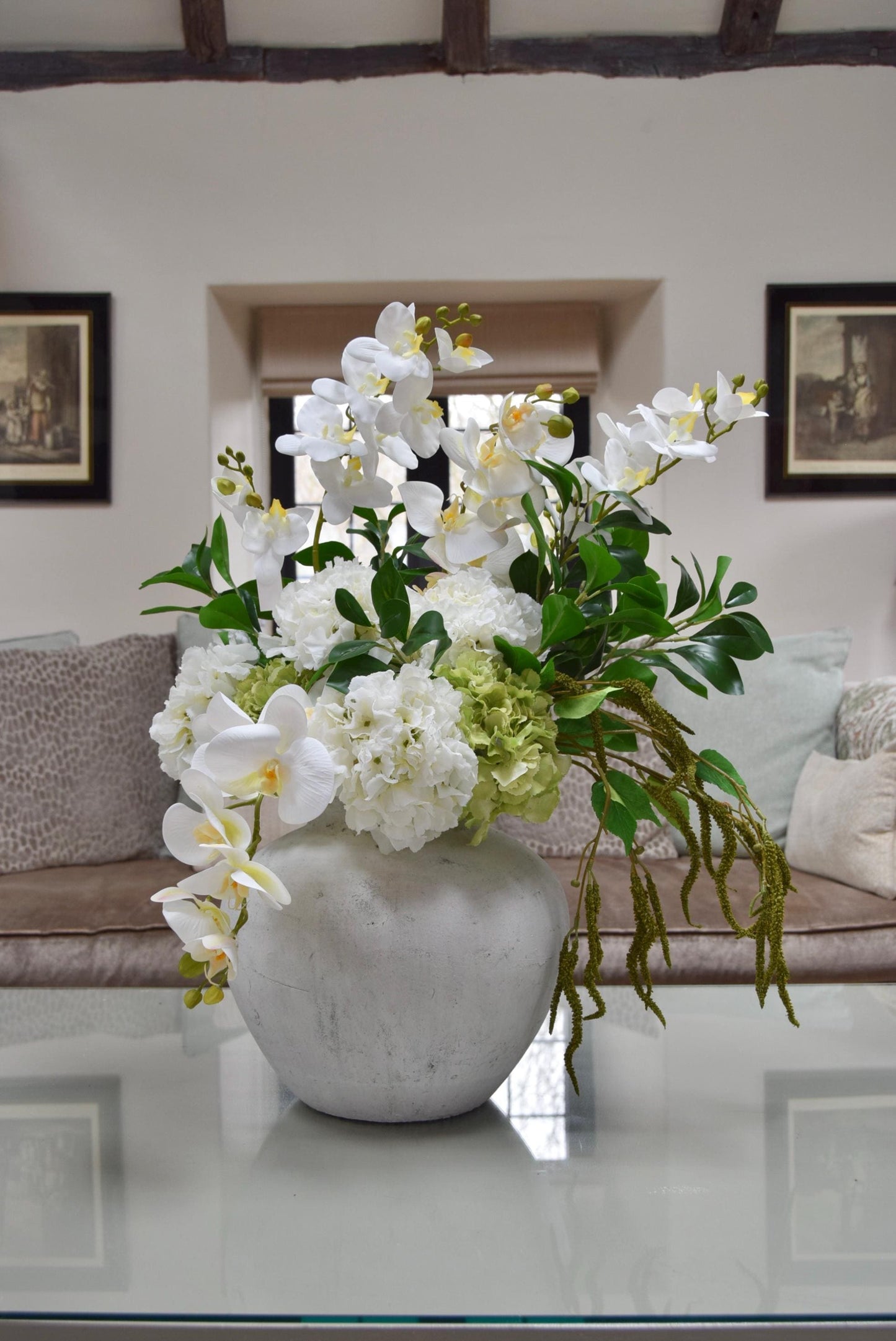 Stone antique vase placed on a kitchen countertop with an arrangement of white orchids, white hydrangeas, green hydrangeas and green foliage. Displayed in a country style kitchen for home decor.