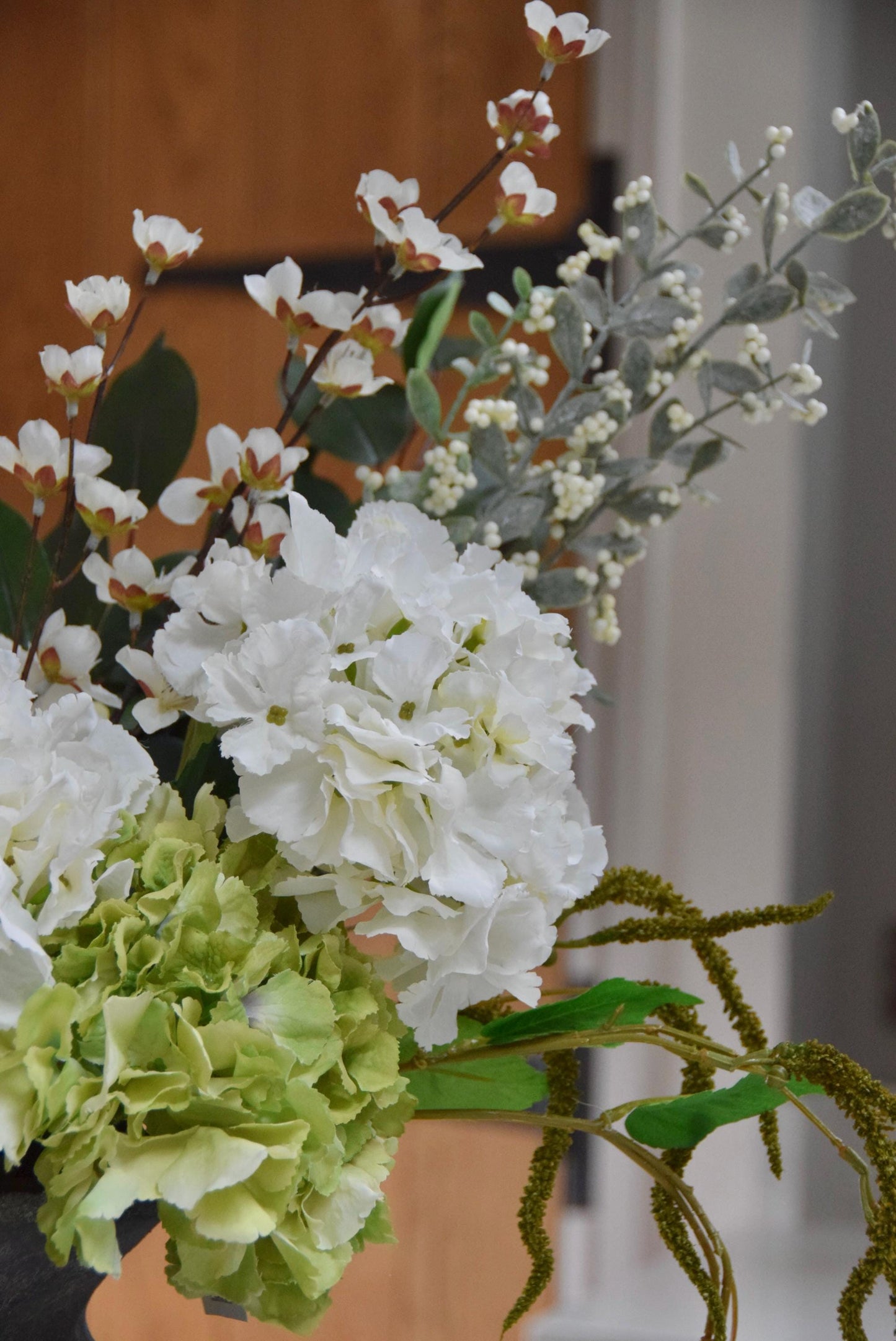 Grey vase placed on a kitchen countertop with a mixture of green and white hydrangeas with lots of mixed foliage. Displayed in a country style kitchen for home decor.