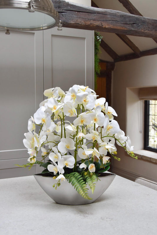 Silver ark bowl placed on a kitchen counter top with an arrangement of white orchids. Arranged in a country style kitchen for home decor.
