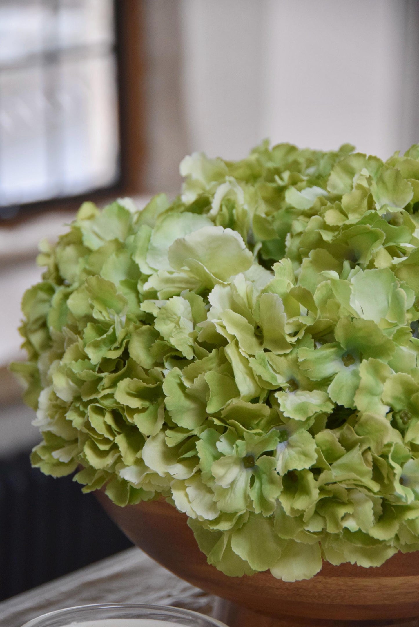 Wooden footed chalice bowl placed on a kitchen counter top with an arrangement of green hydrangeas. Displayed in a country style kitchen for home decor.