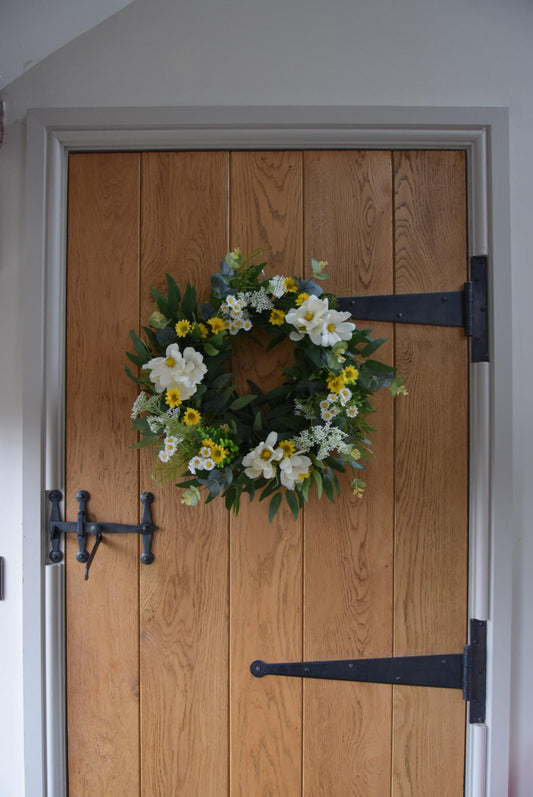 Wreath hanging on rustic country style wooden door with a mixture of daisies, wildflowers, mini bud sprays and greenery. Displayed on a barn door for home decor.