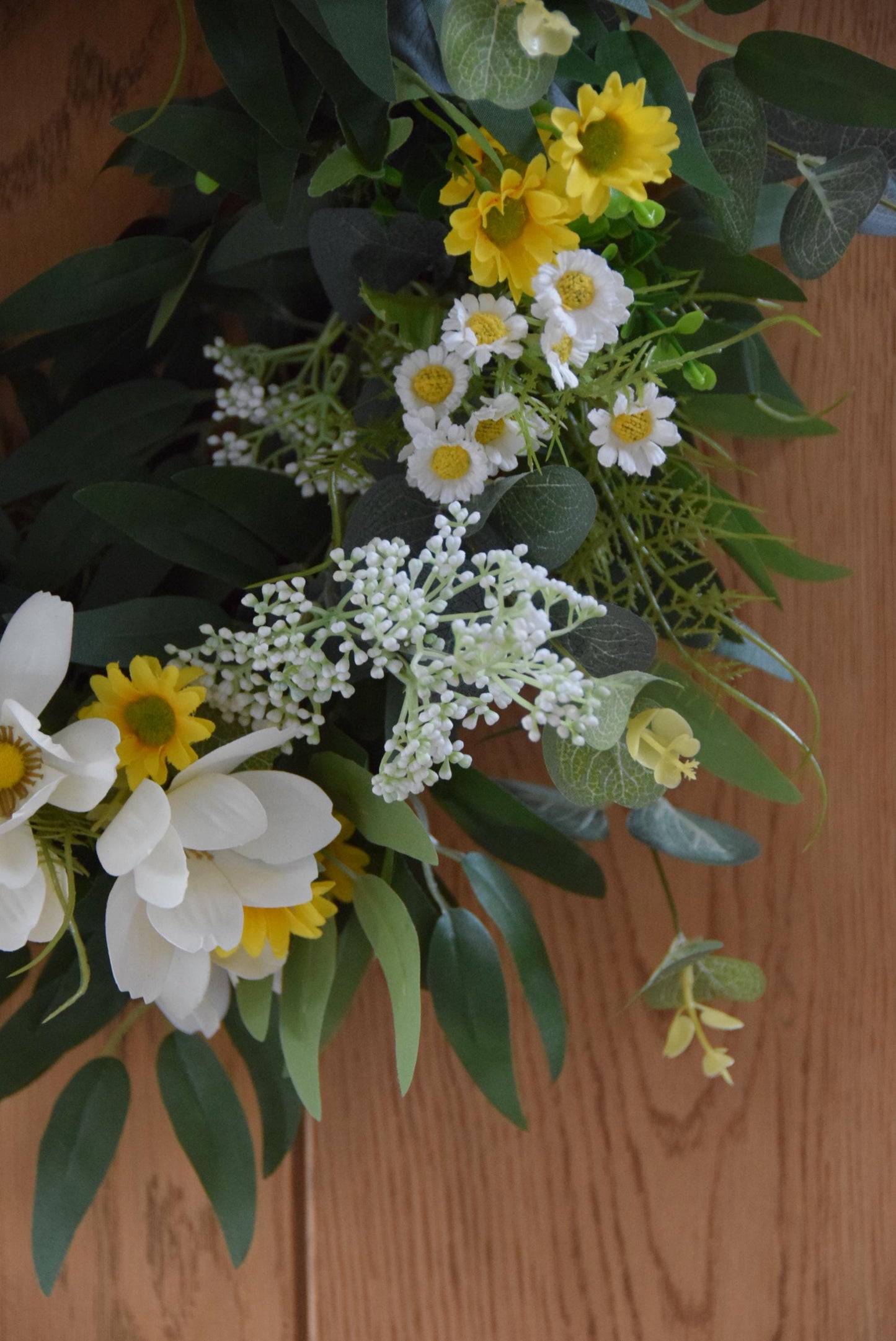 Wreath hanging on rustic country style wooden door with a mixture of daisies, wildflowers, mini bud sprays and greenery. Displayed on a barn door for home decor.