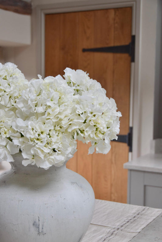 White stone vase on kitchen countertop featuring white hydrangeas. Displayed in a country style kitchen for home decor.