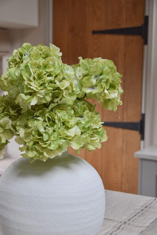 White round vase on kitchen countertop featuring green hydrangeas. Displayed in a country style kitchen for home decor.