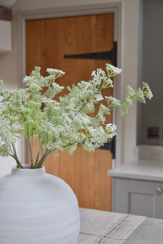 White round vase placed on a kitchen countertop with a bunch of white mini bud stems displayed in a country style kitchen for home decor.