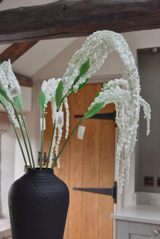 Tall black vase on a kitchen countertop with long white amaranthus trailing stems. Set in a country style kitchen for home decor.