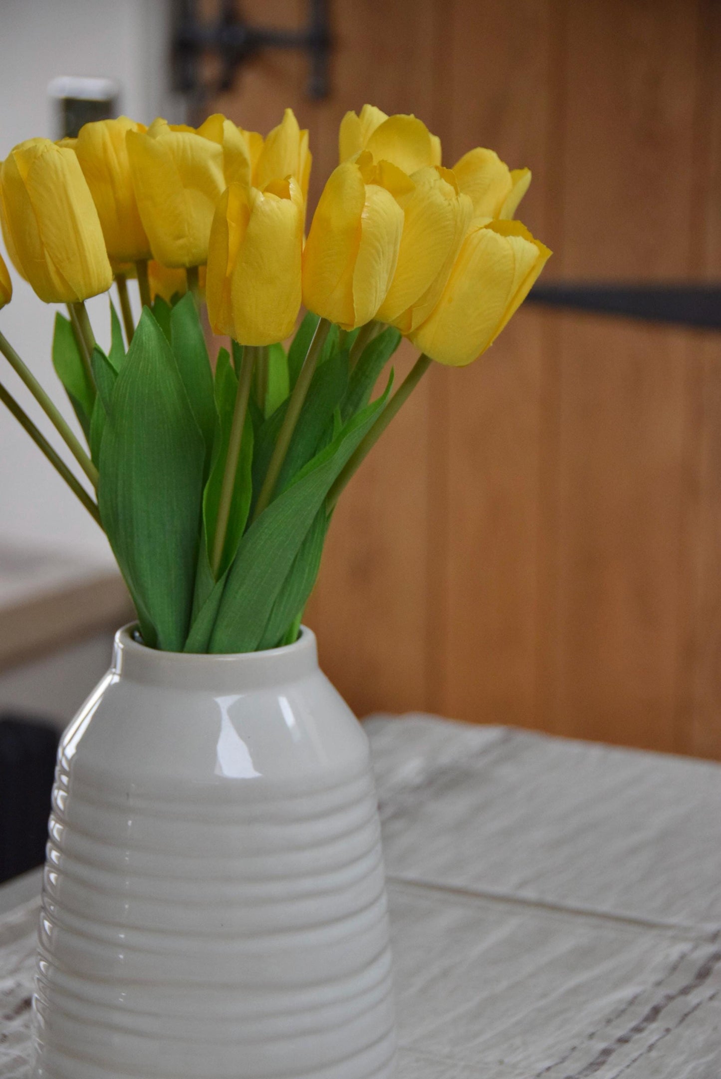 Yellow tulips set in a cream vase on a kitchen counter top in a country style kitchen for home decor