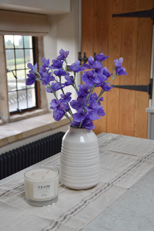 Purple sweet peas set in a cream vase on a kitchen countertop in a country style house for home decor.