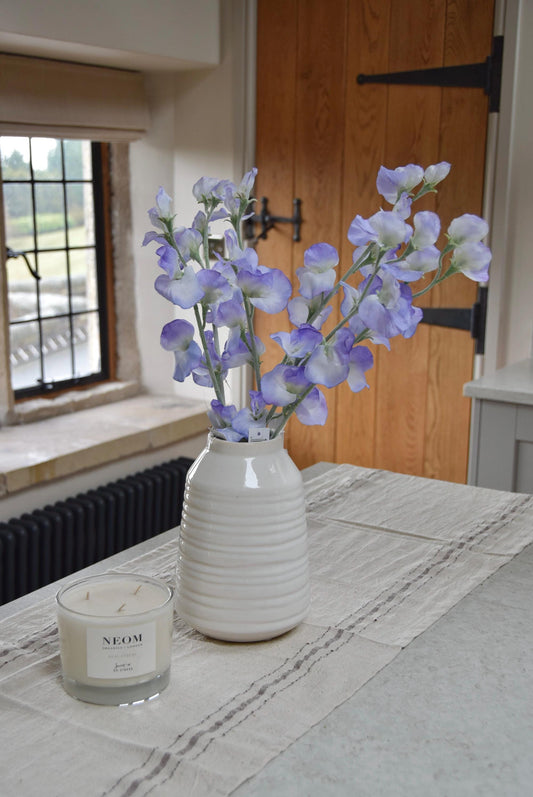 Lilac sweet peas set in a cream vase on a kitchen countertop in a country style house for home decor.