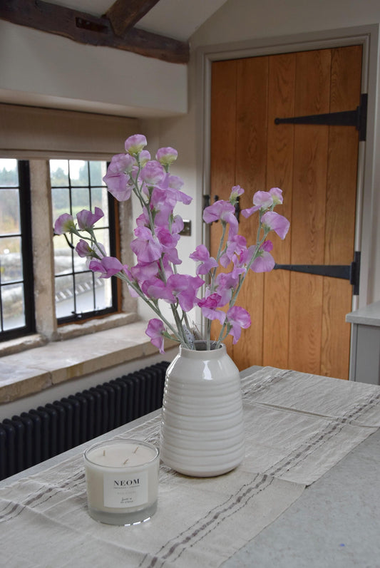 Pink sweet peas set in a cream vase on a kitchen countertop in a country style house for home decor.