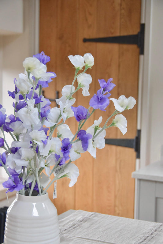 Purple and white sweet peas set in a cream vase on a kitchen countertop in a country style kitchen for home decor.