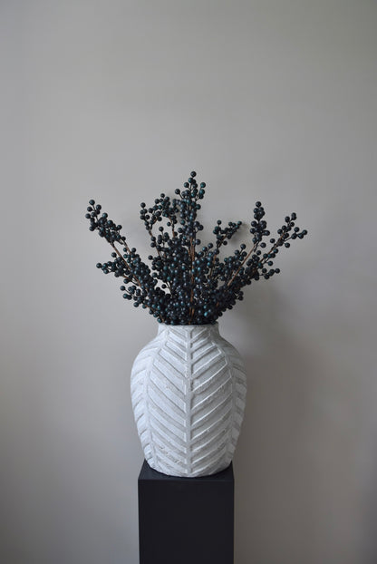 Stone chevron style vase placed on a black pedestal displaying some blueberry stems.