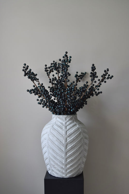 Stone chevron style vase placed on a black pedestal displaying some blueberry stems.