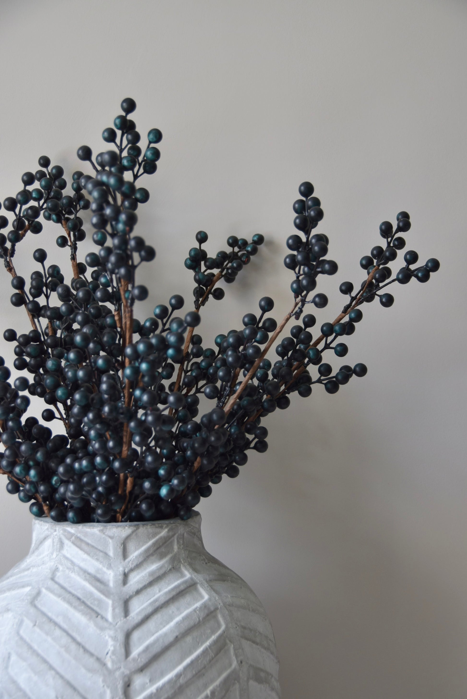 Stone chevron style vase placed on a black pedestal displaying some blueberry stems.