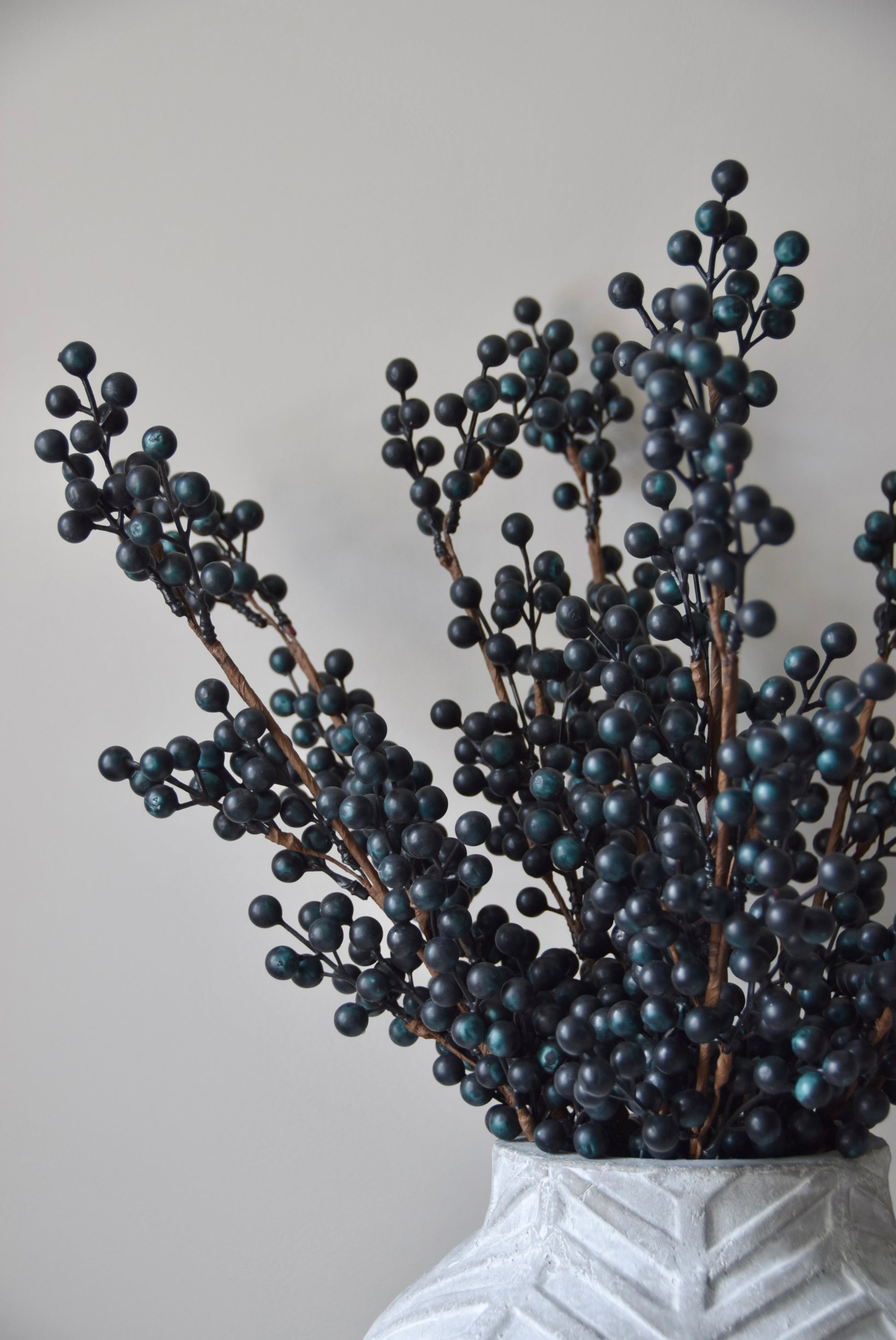 Stone chevron style vase placed on a black pedestal displaying some blueberry stems.