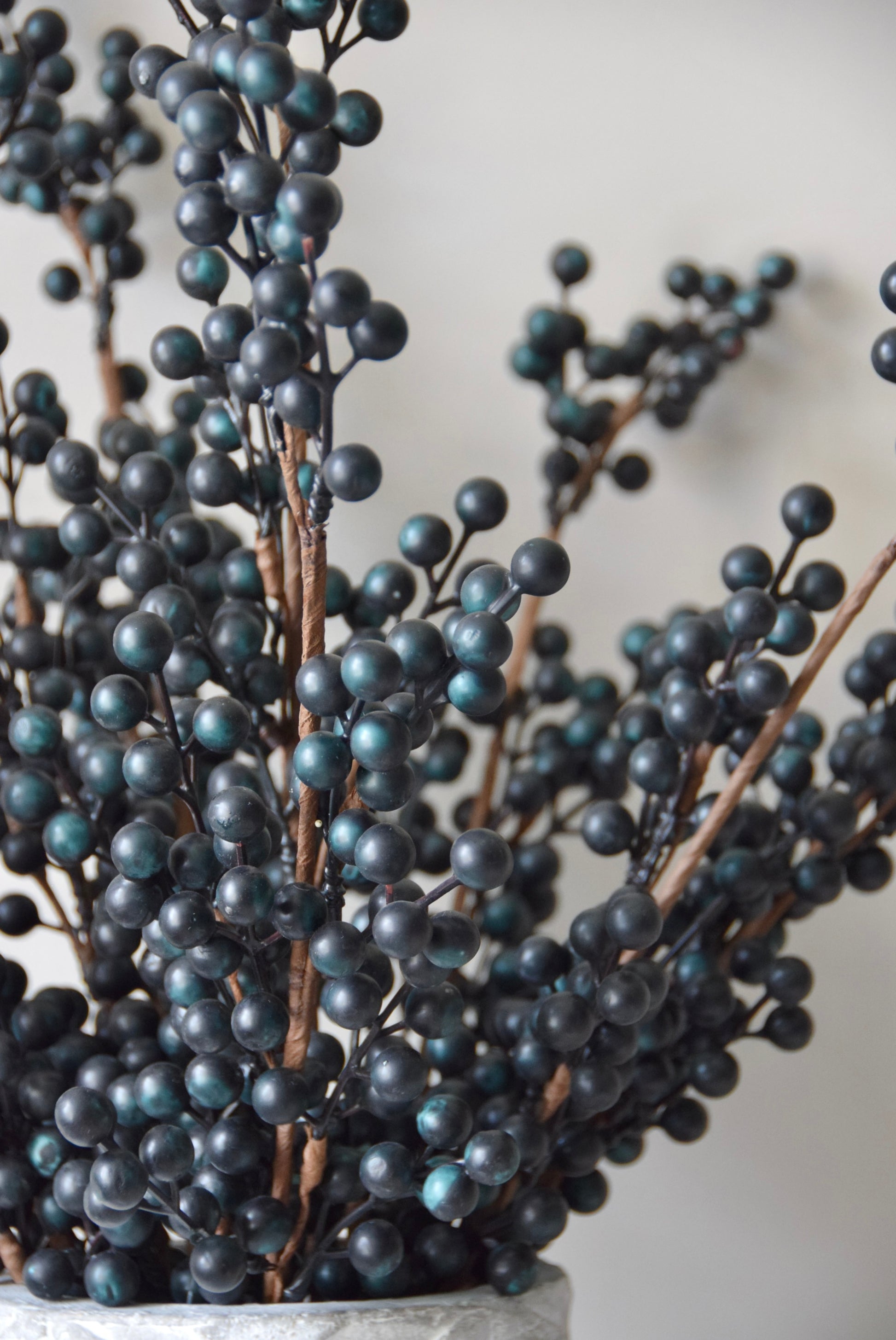 Stone chevron style vase placed on a black pedestal displaying some blueberry stems.