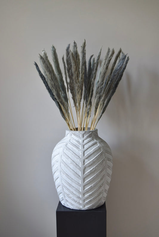 Grey reed pampas stems displayed in a chevron stone vase on a black pedestal.