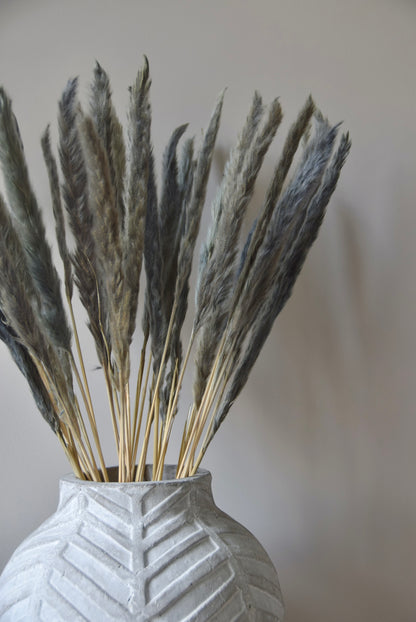 Grey reed pampas stems displayed in a chevron stone vase on a black pedestal.