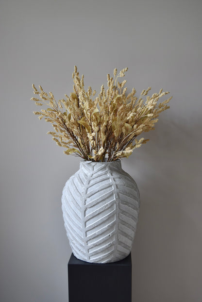 Dried-look grain sorghum spray displayed in a stone chevron style vase placed on a black pedestal.